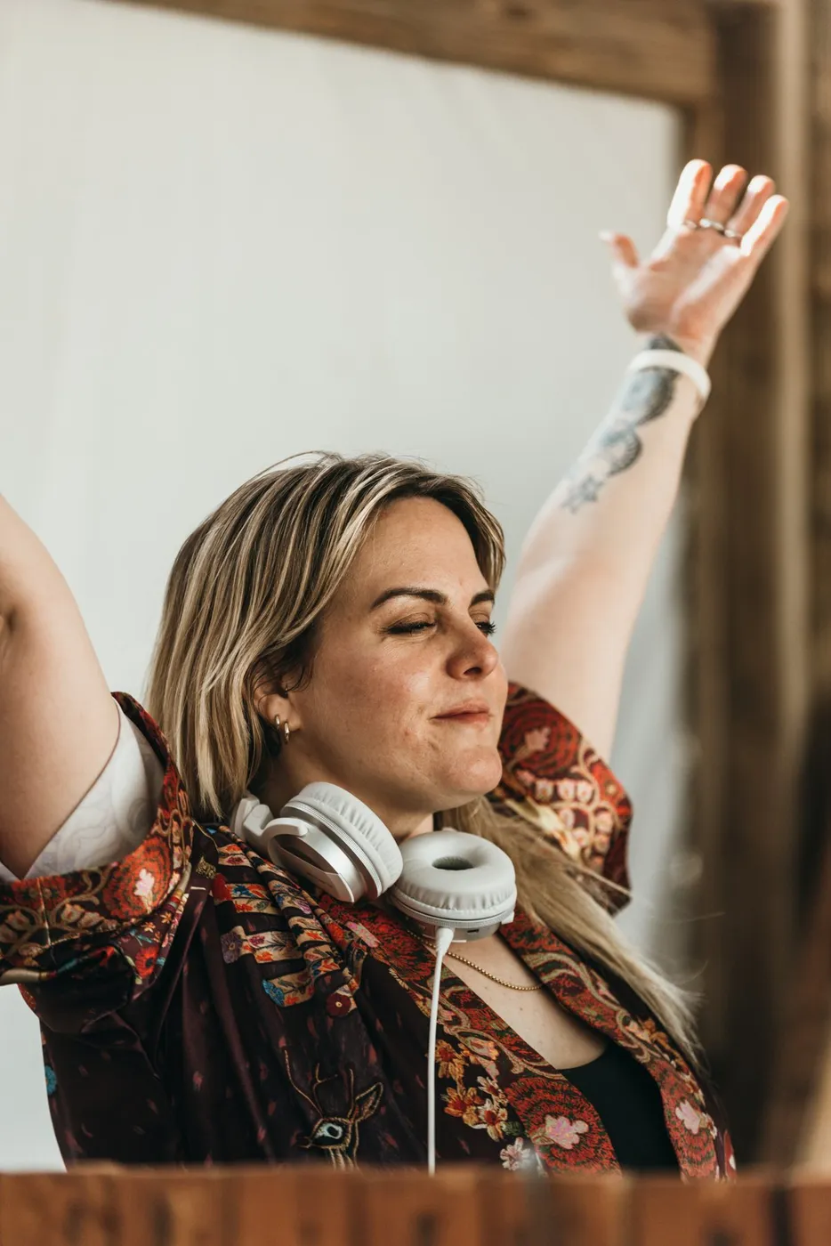A DJ with headphones round her neck throwing an arm in the air at the Oasis booth