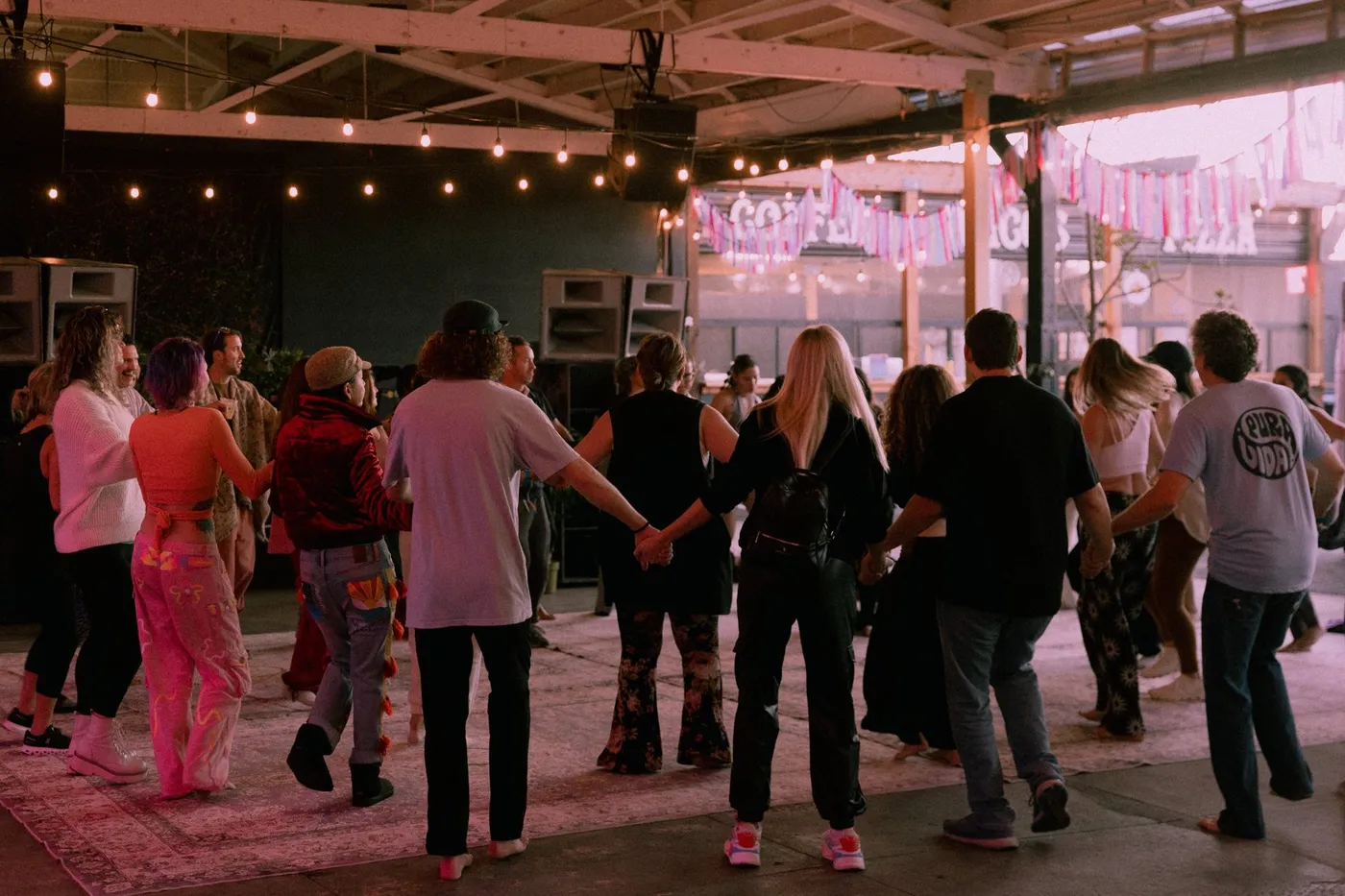 A crowd dancing hand in hand under string lights at Press Pause