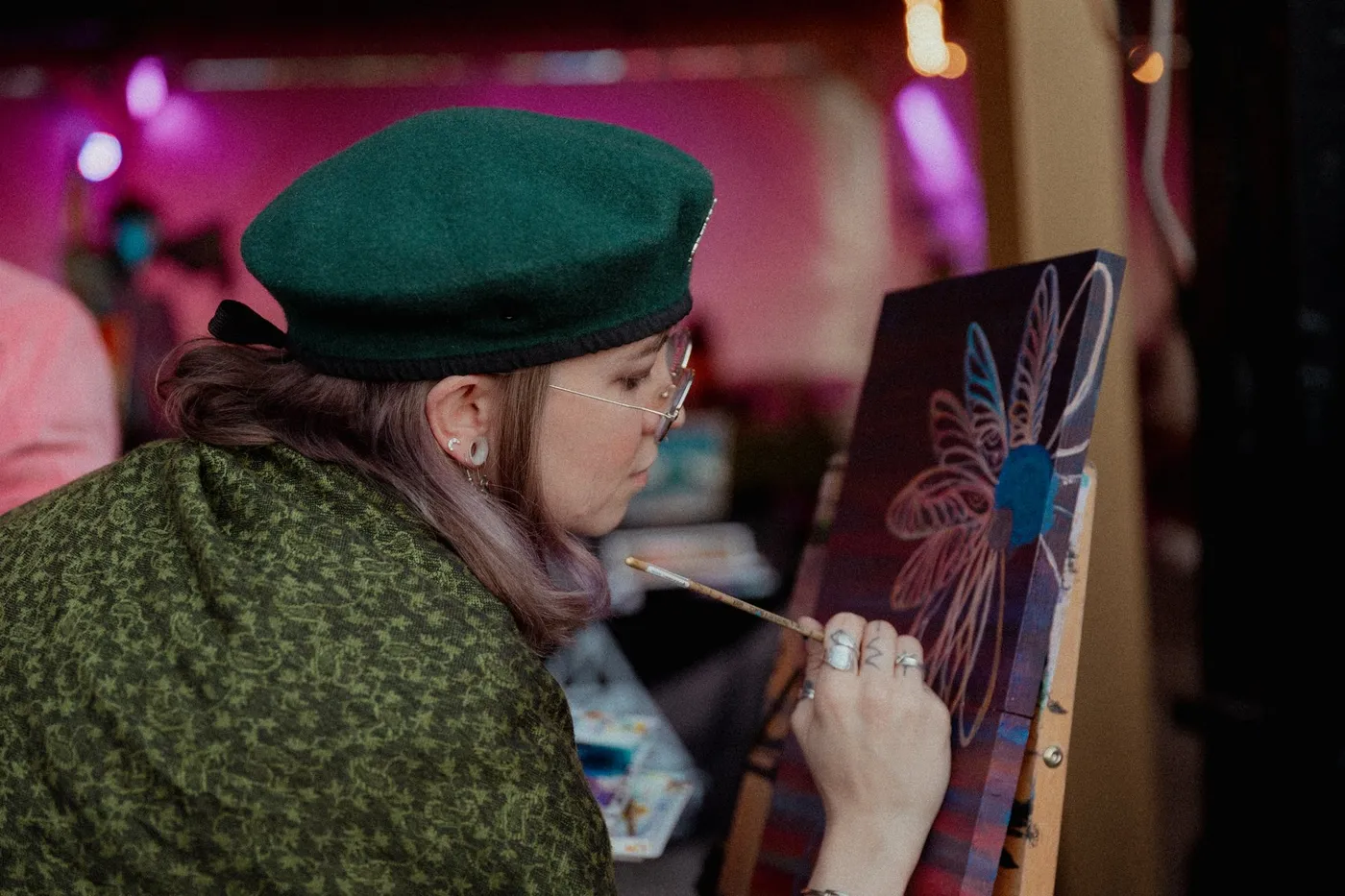 An artist in a green beret painting a canvas live at Press Pause
